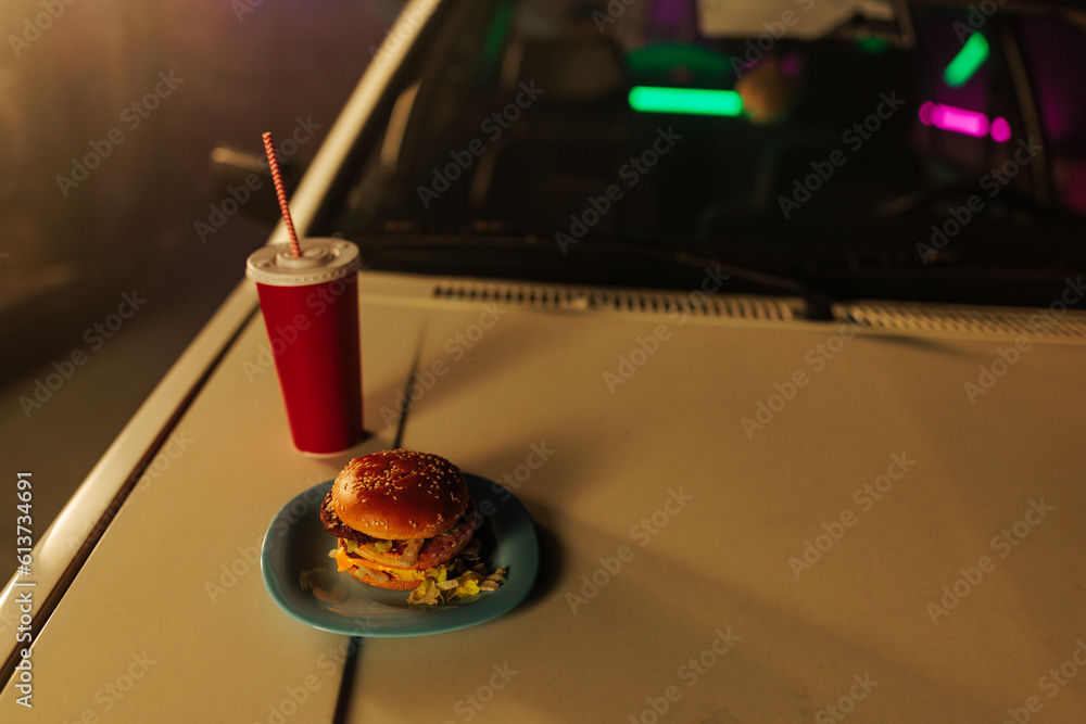 Old timer car with burger and soda on hood.