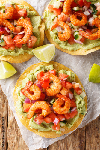 Mexican shrimp tostada flat tacos topped with guacamole and fresh salsa closeup on the wooden table. Vertical top view from above