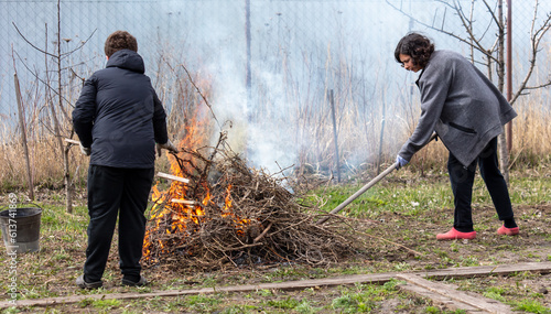 A boy and a woman are burning dry grass in the garden