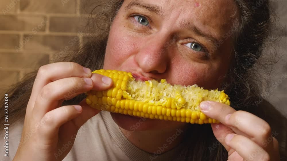 Caucasian woman eats yellow juicy boiled corn with appetite. In the background is a stone gray wall Caucasian woman eats yellow juicy boiled corn with appetite. In the background is a stone gray wall