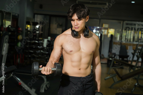 Asian handsome man with perfect body playing weight training at fitness center.