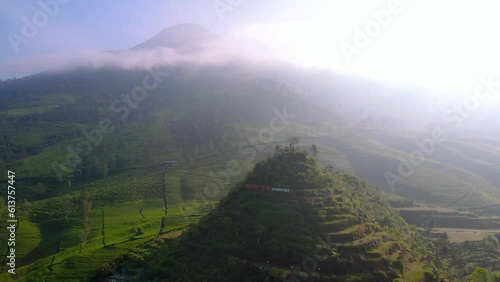 Aerial view of Gunung Cilik at Wonosobo, Central Java, Indonesia. Nature tropical landscape of small mountain surrounded by plantation with huge mountain on the background in the misty morning photo