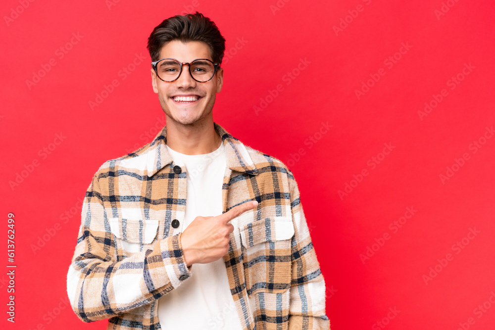 Young caucasian handsome man isolated on red background pointing to the side to present a product Young caucasian handsome man isolated on red background pointing to the side to present a product