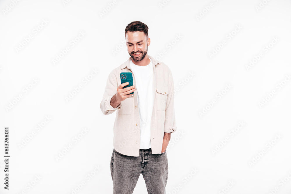 Handsome smiling stylish hipster lambersexual model. Sexy man in white T-shirt and jeans. Fashion male isolated on white background in studio. Holding smartphone, using cellphone apps, mobile phone Handsome smiling stylish hipster lambersexual model. Sexy man in white T-shirt and jeans. Fashion male isolated on white background in studio. Holding smartphone, using cellphone apps, mobile phone