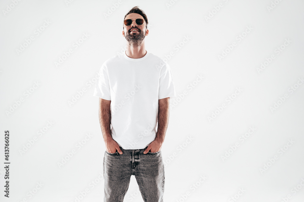 Portrait of handsome smiling stylish hipster lambersexual model. Sexy man dressed in white T-shirt and jeans. Fashion male isolated on white background in studio. In sunglasses Portrait of handsome smiling stylish hipster lambersexual model. Sexy man dressed in white T-shirt and jeans. Fashion male isolated on white background in studio. In sunglasses