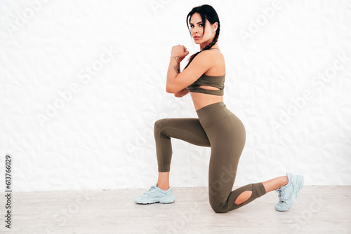 Fitness woman in sports clothing. Sexy young beautiful model with perfect body wearing sportswear. Female making exercises at home in white interior. Stretching out before training. Makes lunges