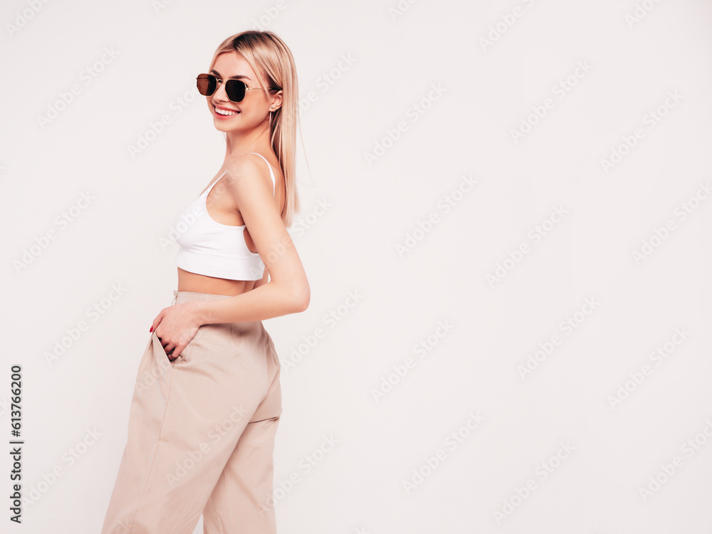 Young beautiful smiling blond female in trendy summer white top t-shirt and beige trousers clothes. Sexy carefree woman isolated on white background in studio. Positive model. In sunglasses Young beautiful smiling blond female in trendy summer white top t-shirt and beige trousers clothes. Sexy carefree woman isolated on white background in studio. Positive model. In sunglasses