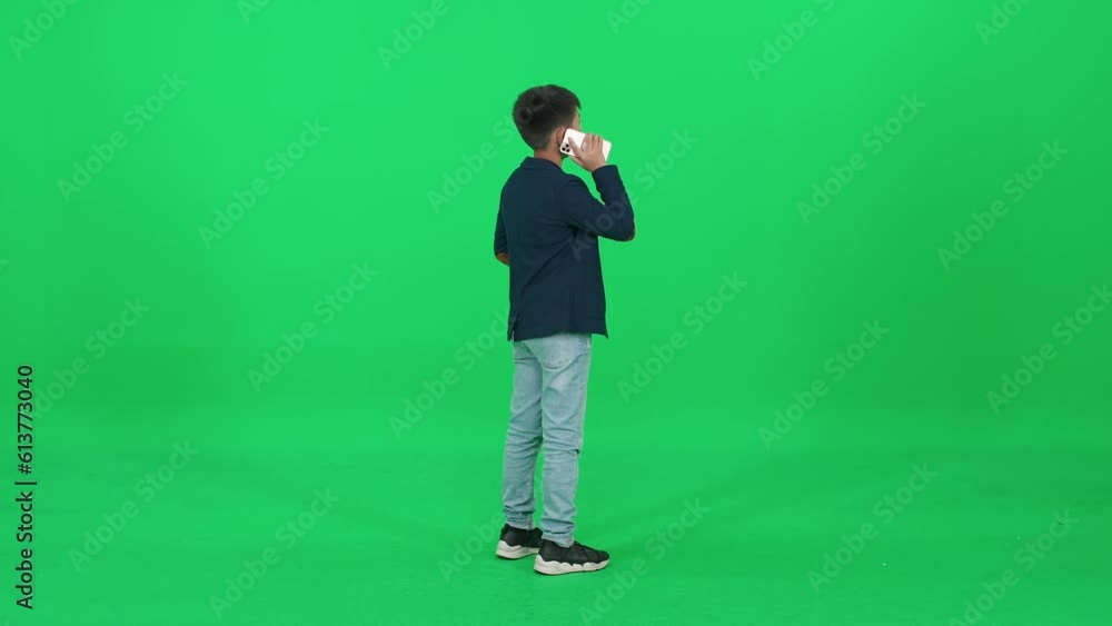Back view, Asian schoolboy in a suit standing on a green background and talking on a mobile phone, template on a chromakey. Back view, Asian schoolboy in a suit standing on a green background and talking on a mobile phone, template on a chromakey.