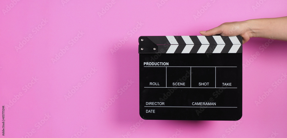 Hands are holding a black clapper board or movie slate on pink background.