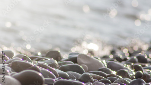 Sea pebble stones and water, defocused sun lights bokeh nature background. Natural beach stones background, wallpaper soft focus.