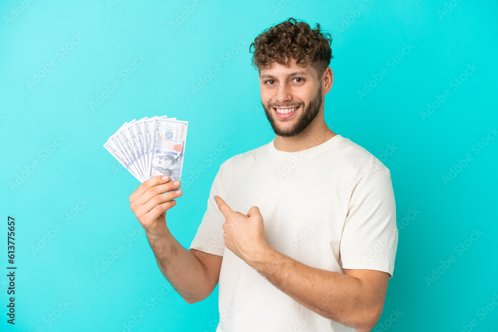 Young caucasian man taking a lot of money isolated on blue background pointing back Young caucasian man taking a lot of money isolated on blue background pointing back