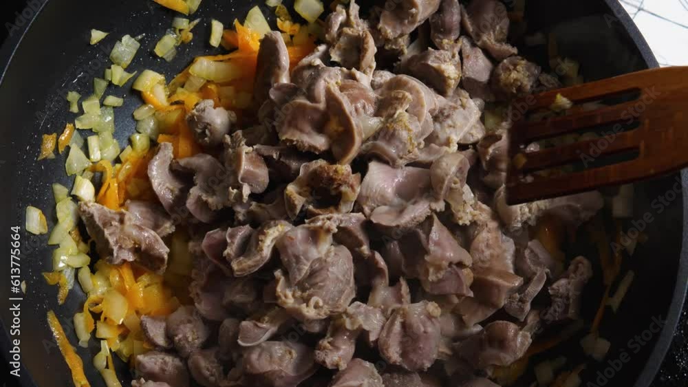 Top view of a woman's hand in a wok with fried onions and carrots poured Chicken Gizzard and stirred with a wooden spatula. Close-up. Cooking in the Asian style Top view of a woman's hand in a wok with fried onions and carrots poured Chicken Gizzard and stirred with a wooden spatula. Close-up. Cooking in the Asian style
