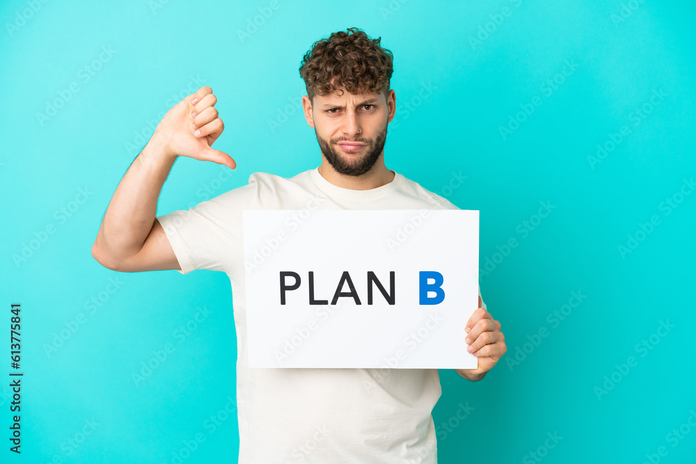 Young handsome caucasian man isolated on blue background holding a placard with the message PLAN B and doing bad signal Young handsome caucasian man isolated on blue background holding a placard with the message PLAN B and doing bad signal