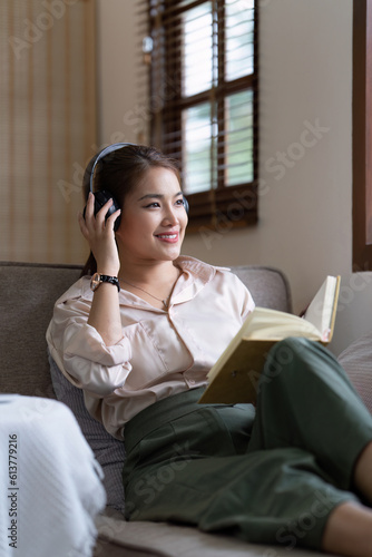 Young relaxed smiling pretty woman relaxing sitting on sofa at home. Female feeling joy enjoying and reading book on cozy couch © itchaznong