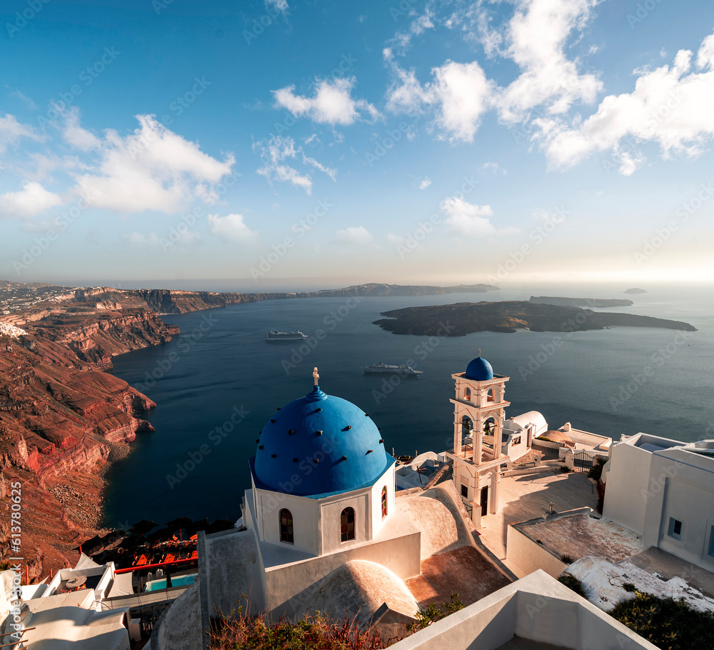 Golden hour image of white and blue church with view on the caldera cliff and cruise ships on the Greek island of Santorini