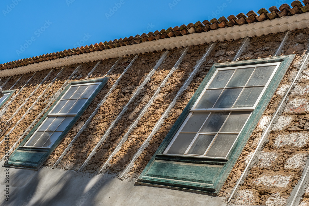 Obraz premium Facade of old house under construction, half whitewashed, in the city of La Laguna. Green wooden windows. Sunny day. Colorful houses Tenerife, Canary Islands, Spain.