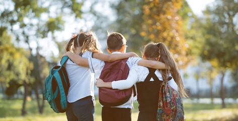 school friends a boy and two girls with school backpacks on their backs walk after class