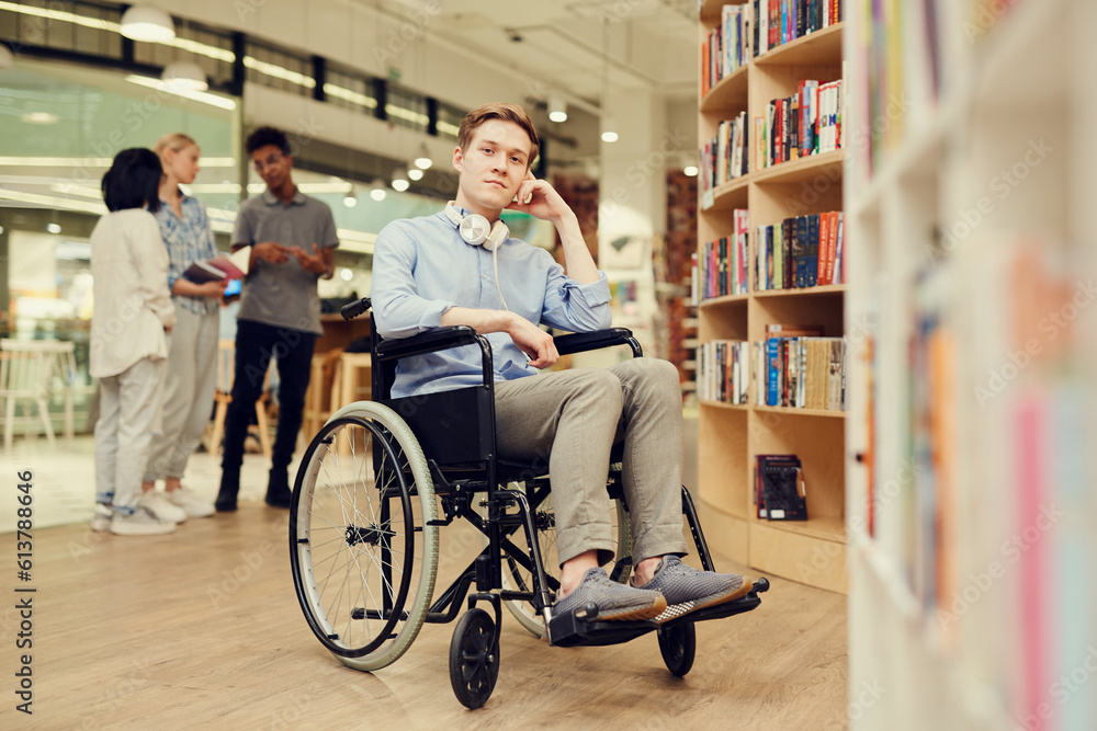 Obraz premium Portrait of content young person with disability student boy with headphones on neck sitting in wheelchair while spending leisure in library