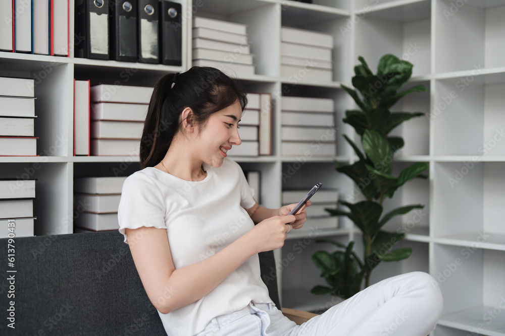 Young relaxed smiling pretty woman relaxing sitting on sofa at home. Female feeling joy enjoying with mobile phone on cozy couch