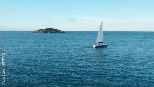 Small Sailboat Sails at Joao Fernandes Beach, Rio de Janeiro Brazil, Tropical Blue Water and Green Lonely Island in the Ocean, Aerial Drone Shot photo