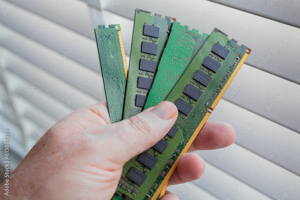 A hand holding several desktop computer RAM chips with some white blinds in the background.