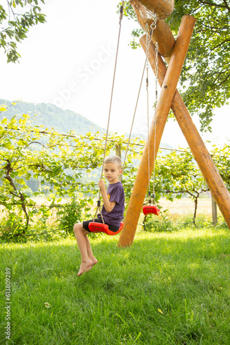 A boy of seven years old rides on a swing in the garden photo