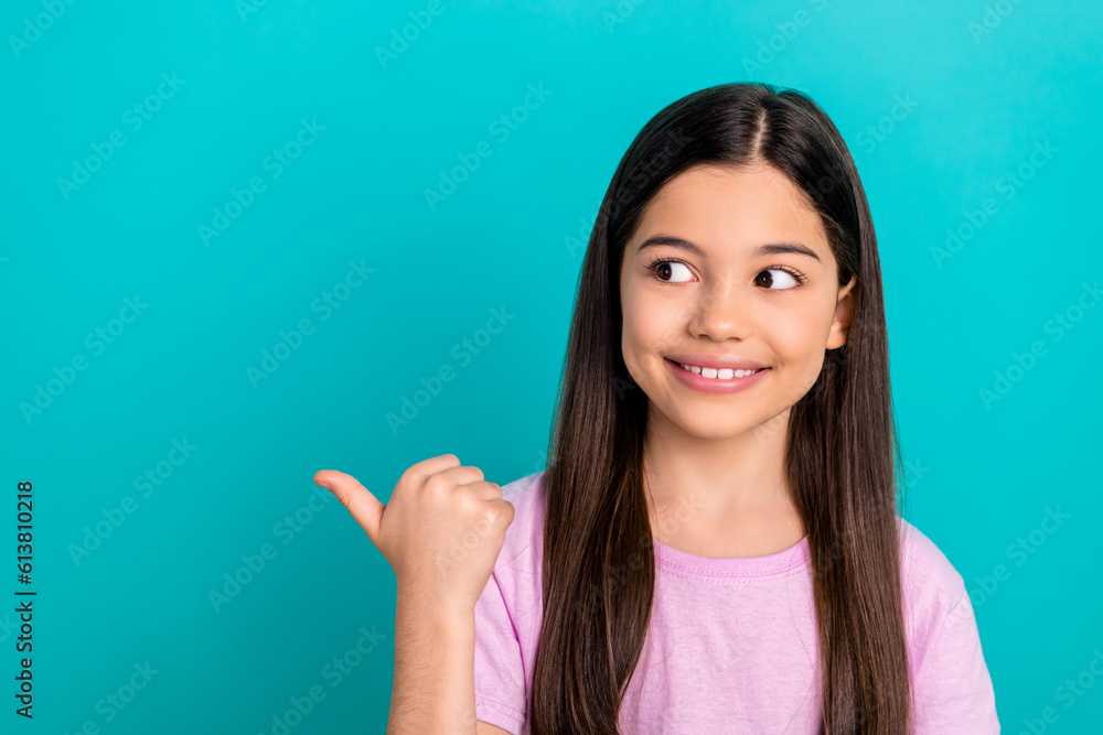 Photo of shiny thoughtful little child dressed pink t-shirt looking showing thumb empty space isolated teal color background Photo of shiny thoughtful little child dressed pink t-shirt looking showing thumb empty space isolated teal color background