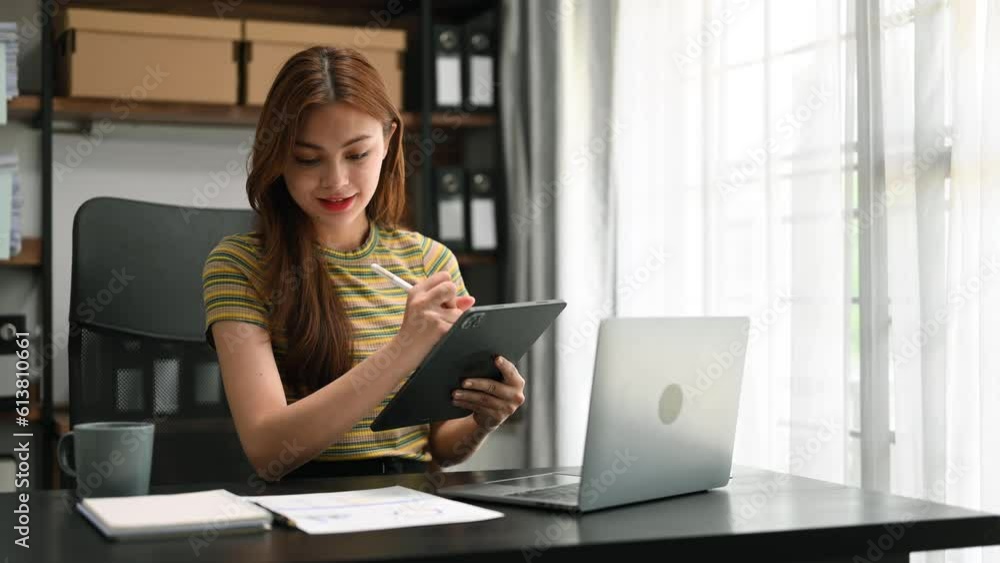 Young beautiful woman typing on tablet and laptop while sitting at the working wooden table modern office. Young beautiful woman typing on tablet and laptop while sitting at the working wooden table modern office.