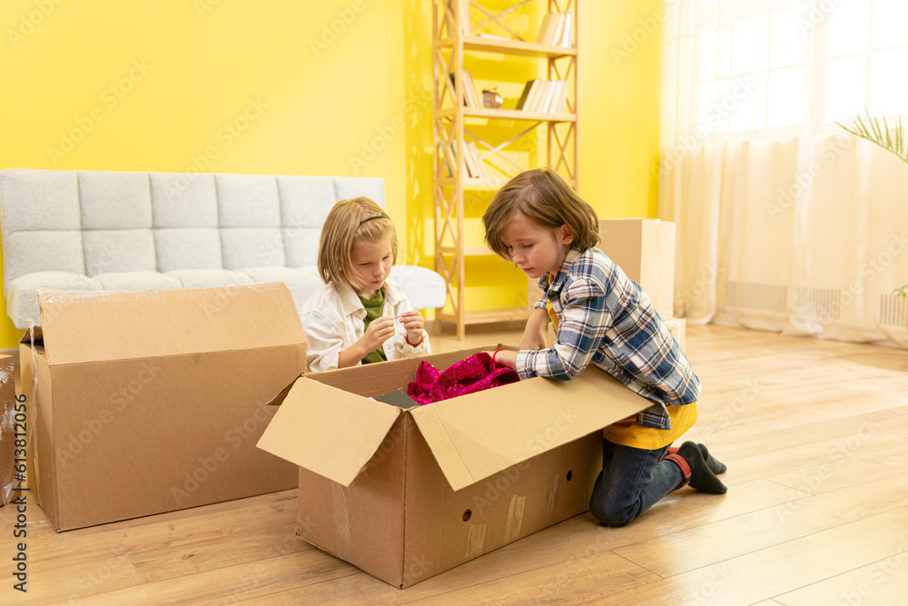 Excited kids laughing playing in new home carrying boxes, happy family with children enjoying relocation, small girl and boy having fun in living room helping parents to pack, moving day concept Excited kids laughing playing in new home carrying boxes, happy family with children enjoying relocation, small girl and boy having fun in living room helping parents to pack, moving day concept