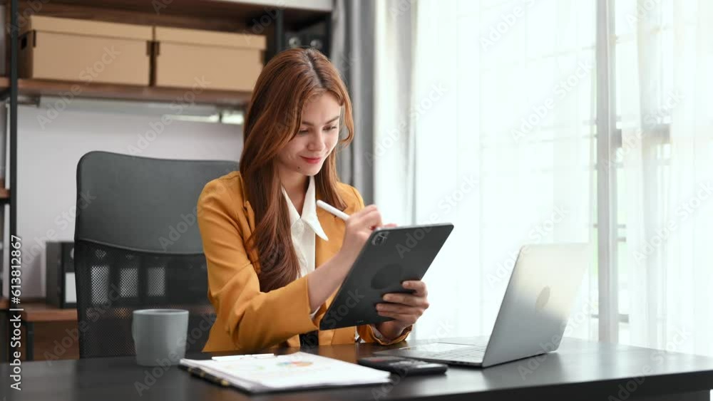 Young beautiful woman typing on tablet and laptop while sitting at the working wooden table modern office. Young beautiful woman typing on tablet and laptop while sitting at the working wooden table modern office.