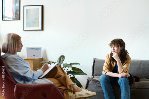 Young woman sitting on sofa and having psycho session with therapist in office
