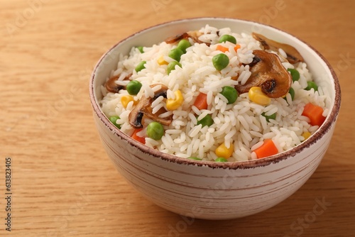Bowl of delicious rice with vegetables on wooden table, closeup