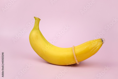 Condom and banana on a pink background close-up.