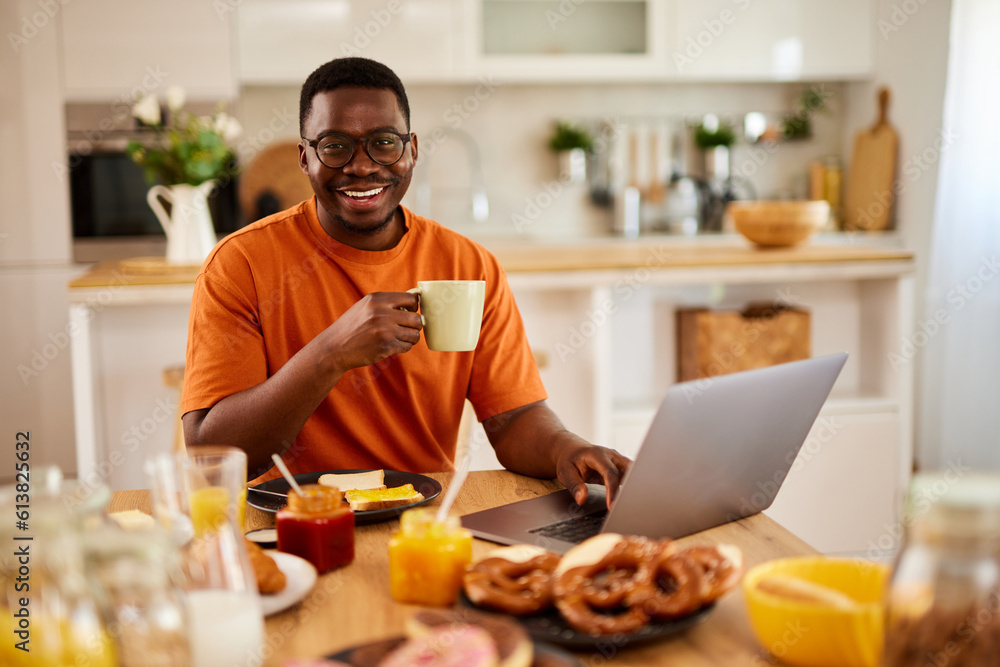 African American man using laptop while enjoying breakfast at home African American man using laptop while enjoying breakfast at home