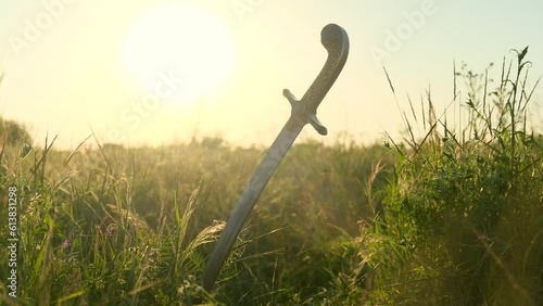 The saber of the Ukrainian Cossacks is stuck in the ground, among the grass, against the background of the sunset. The concept of freedom. photo