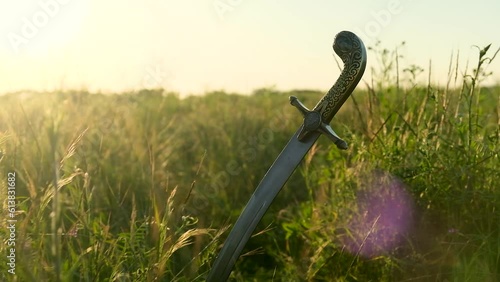 The saber of the Ukrainian Cossacks is stuck in the ground, among the grass, against the background of the sunset. Beautiful bokeh appears in the frame. The concept of freedom. Close-up. photo