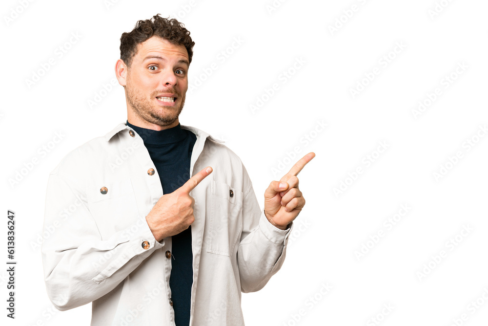 Brazilian man over isolated chroma key background frightened and pointing to the side Brazilian man over isolated chroma key background frightened and pointing to the side
