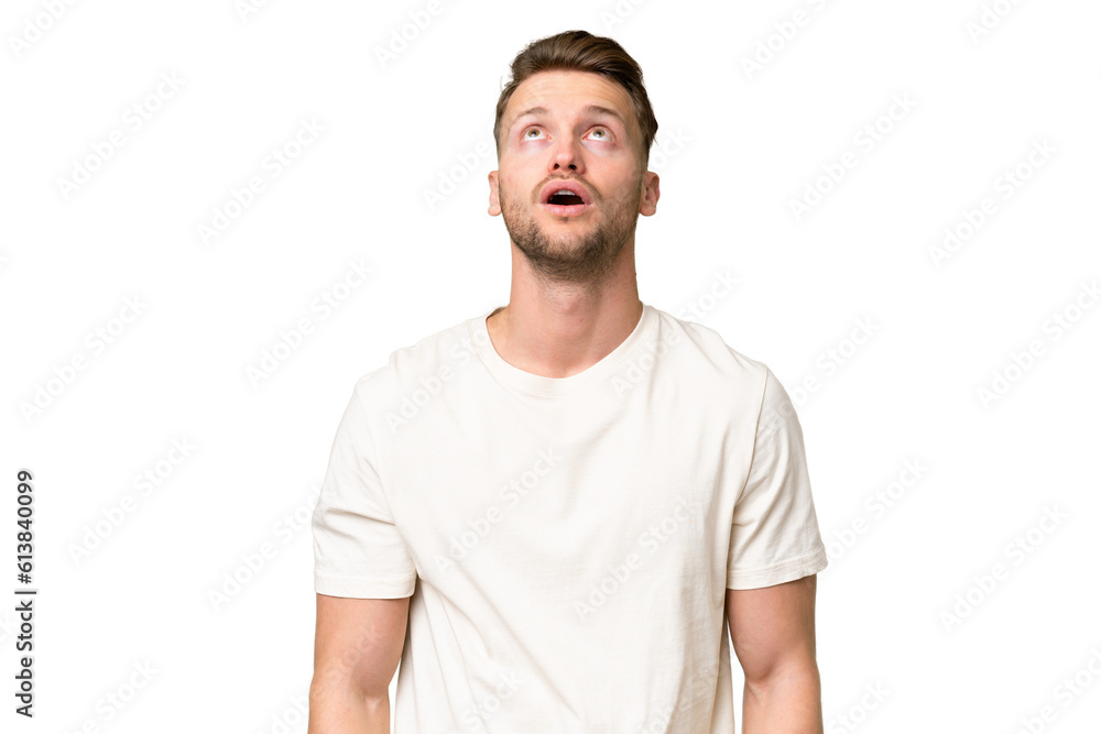 Young blonde caucasian man over isolated background looking up and with surprised expression Young blonde caucasian man over isolated background looking up and with surprised expression