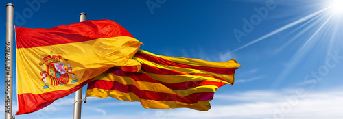 Close-up of a Spanish and Catalan flag (la Rojigualda and Senyera) with flagpole, blowing in the wind on a blue sky with clouds, sunbeams and copy space. photo