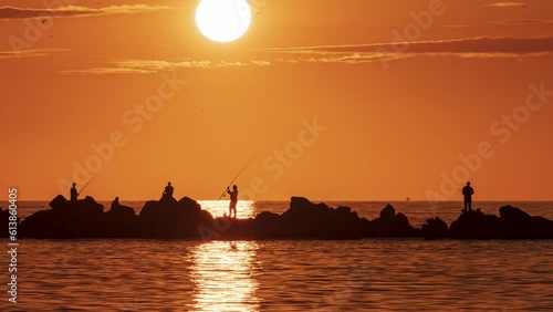 People fishing with a fishing rod at sunset. Impressive image of red sky and sun. photo