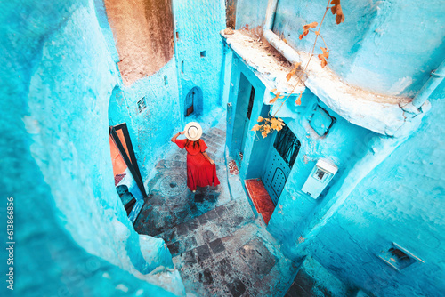 Young woman with red dress visiting the blue city Chefchaouen, Marocco - Happy tourist walking in Moroccan city street - Travel and vacation lifestyle concept