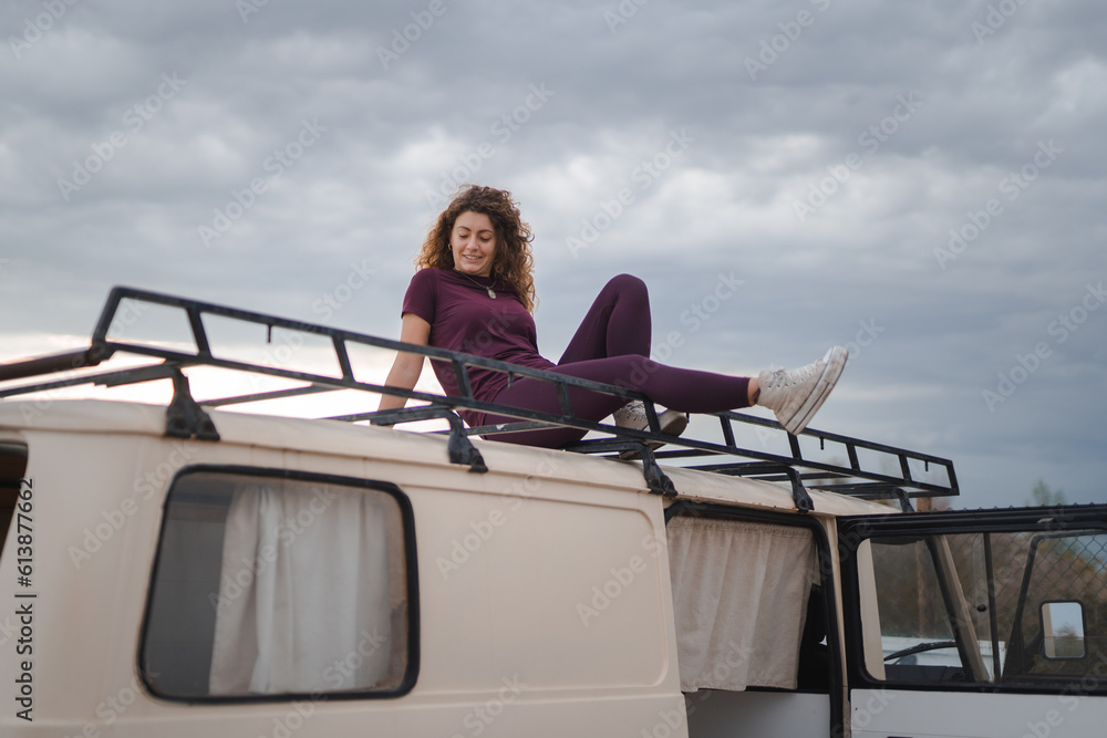 © ADDICTIVE STOCK - Smiling woman resting on van top with luggage carrier