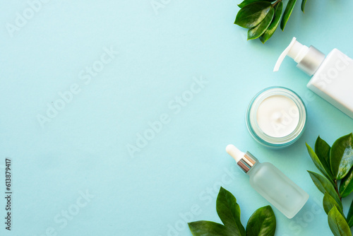 Natural cosmetic products flat lay on blue. Cream and serum with green leaves.
