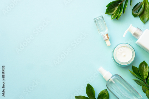 Natural cosmetic products flat lay on blue. Cream and serum with green leaves.