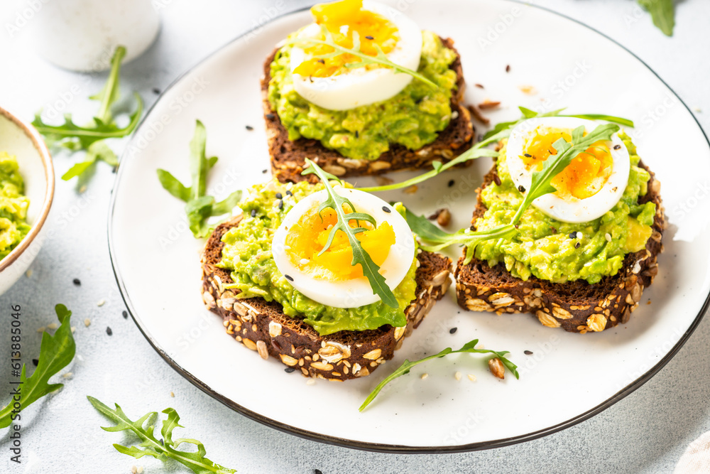 Open sandwich. Whole grain bread with avocado and boiled eggs. Top view on white kitchen table. Open sandwich. Whole grain bread with avocado and boiled eggs. Top view on white kitchen table.