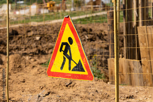 Under construction red and yellow road triangle sign against ground works background 