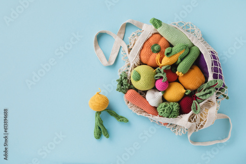 Cute knitting vegetables and fruits for activity, motor and sensory development. Eco friendly toys in cotton bag on blue table.