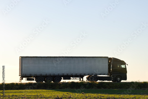 Semi-truck with cargo trailer driving on highway hauling goods in evening. Delivery transportation and logistics concept