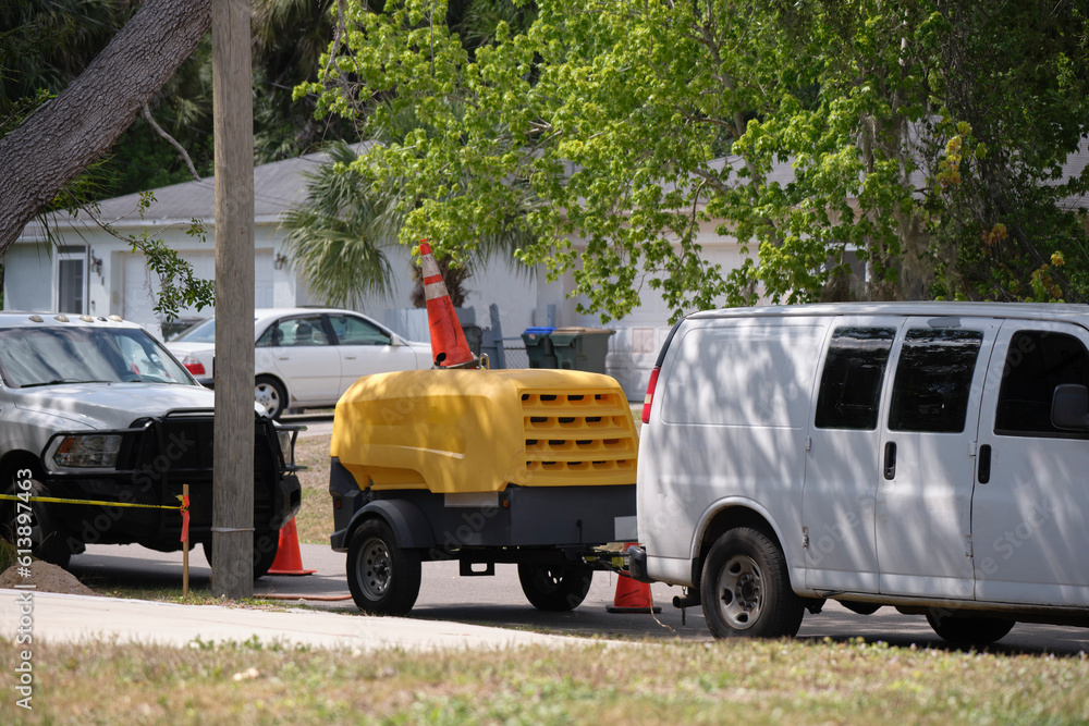 Utility van with yellow compressor trailer with jackhammer machine on road construction site