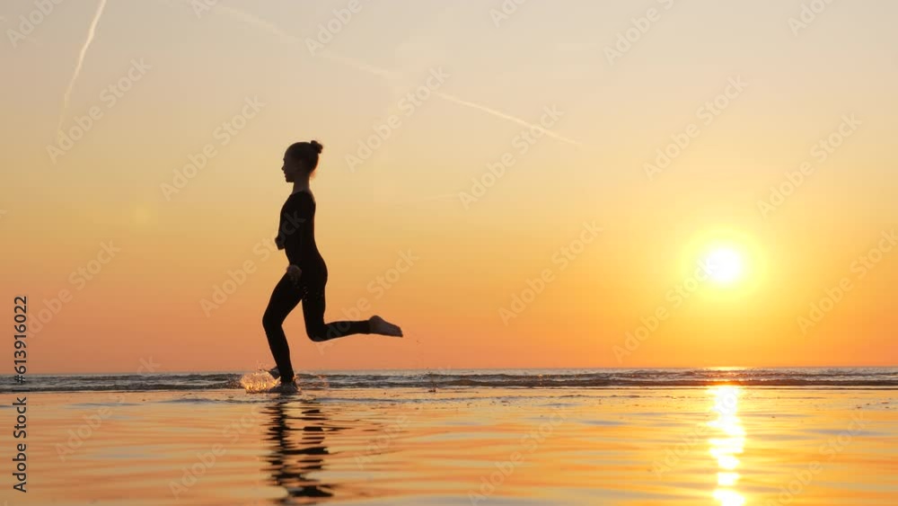 Beautiful shot of young gymnast girl against golden sunset at sea beach. Girl make walkover, stand on hands while moving legs over body. Slender body of teenager athlete against vibrant background Beautiful shot of young gymnast girl against golden sunset at sea beach. Girl make walkover, stand on hands while moving legs over body. Slender body of teenager athlete against vibrant background
